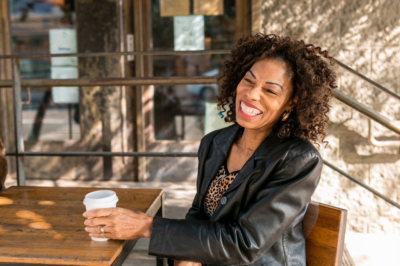 Smiling senior woman relaxing with a coffee at an outdoor cafe, embodying elegant senior style.