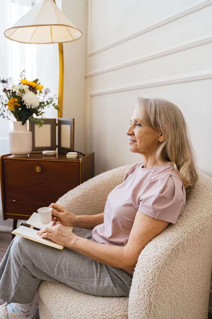 Senior woman enjoying a peaceful moment, holding a cup of coffee, reflecting in a cozy armchair.